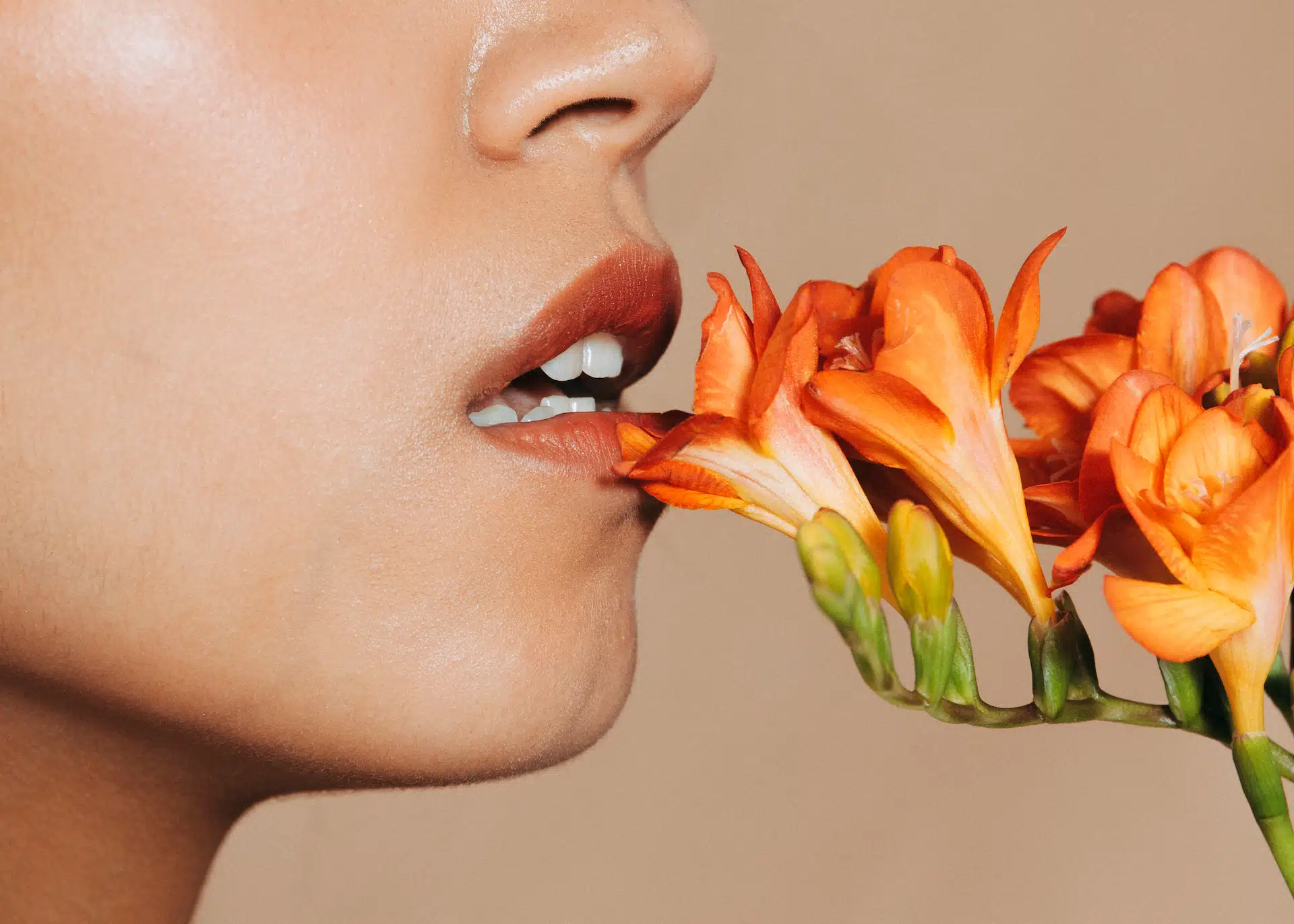 Mujer con labios naturales olfateando flores de color naranja tras hacerse una queiloplastia y eliminación de biopolímeros en la Clínica Fernández Blanco